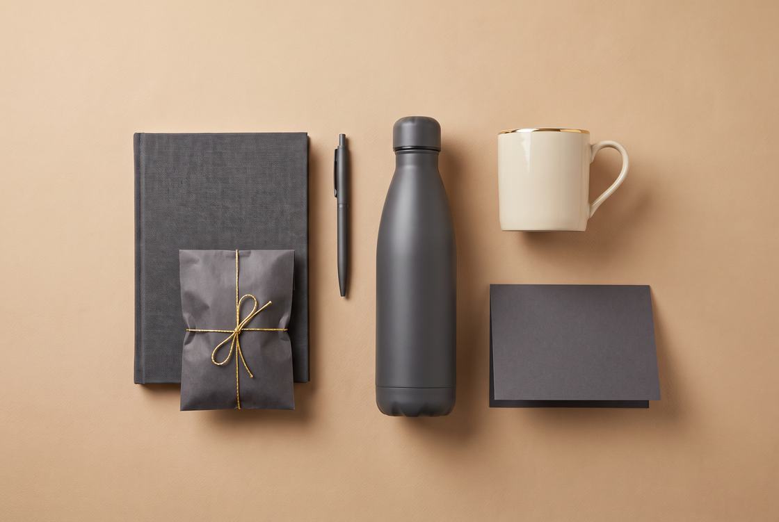 Contents of a corporate employee gift box laid out: notebook, pen, water bottle, mug, wrapped treat and greeting card