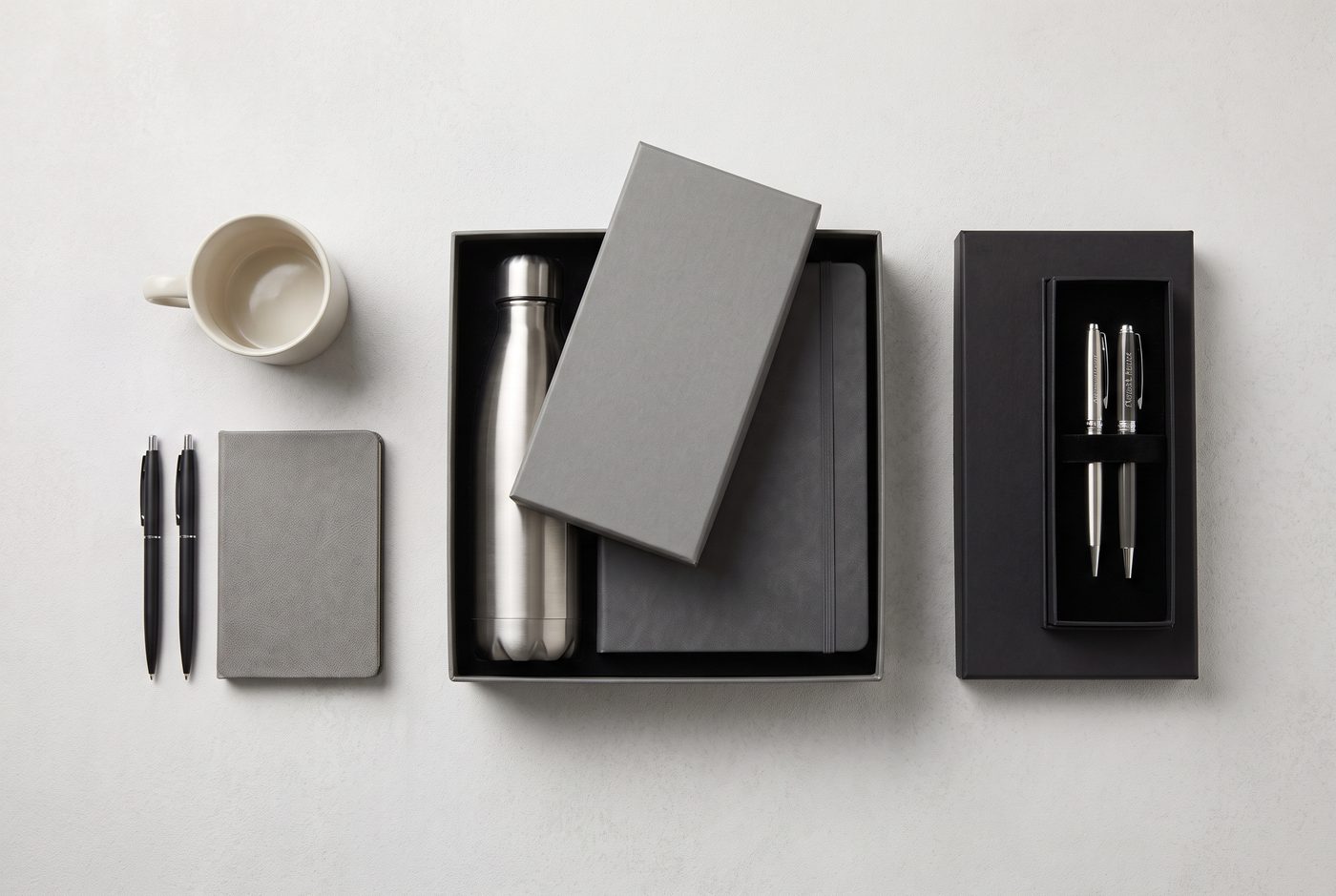Corporate gift budget tiers in Pakistan: mugs and pens, grey rigid gift box with bottle and diary, premium black executive pen set