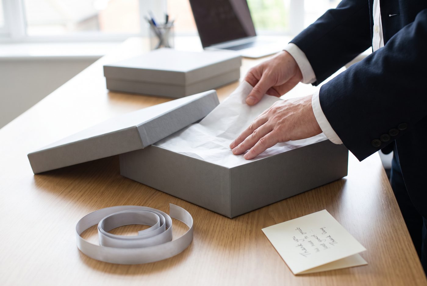 Professional placing tissue paper into a matte grey rigid gift box with a lift-off lid