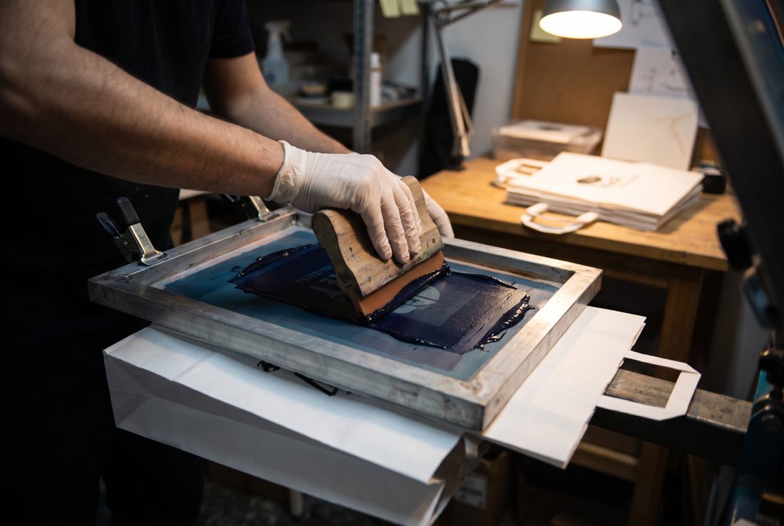 Screen printing a one-colour logo onto paper bags, the standard bulk branding method for corporate gifts in Pakistan